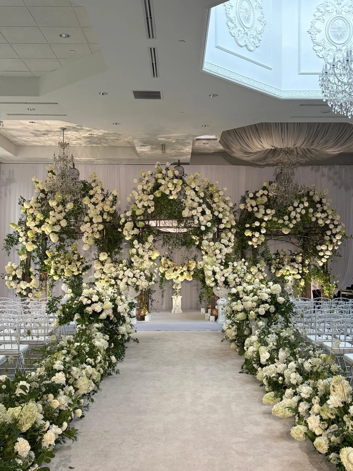 White rose arch aisle installation beneath crystal chandeliers